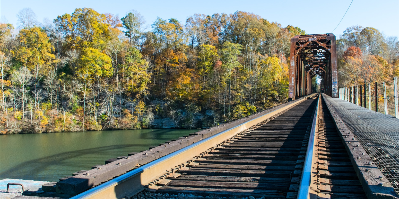 scenic view of railroad bridge over water with trees in the background during autumn